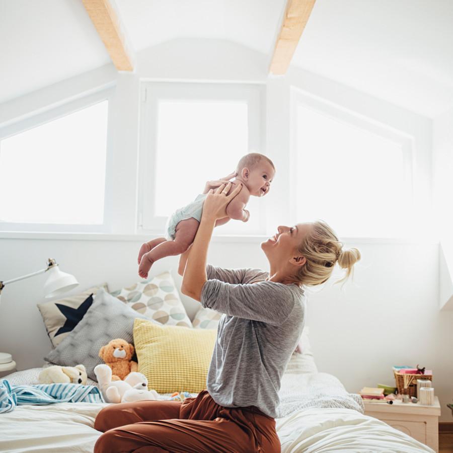 mother lifting up her baby, they are inside a nice nursery room