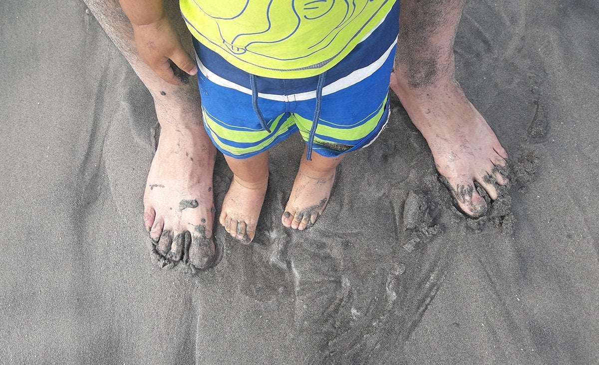 foot of an adult and a baby on the sand