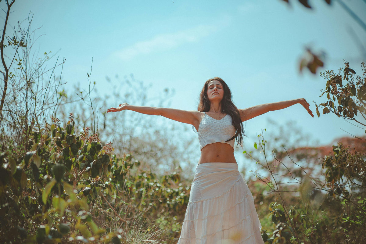 woman wearing white skirt and white top in the field embracing natural beauty with open arms