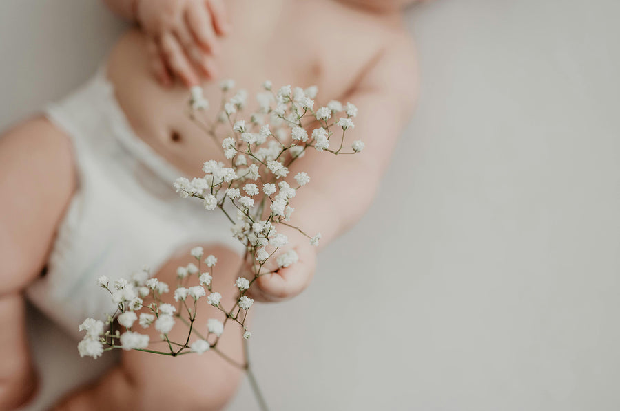 Baby wearing diaper holding white flowers