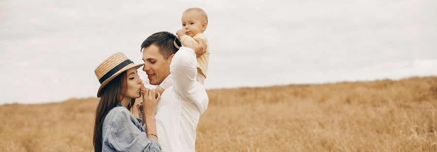 family picture mother kissing her baby foot while the baby is sitting on his fathers shoulder